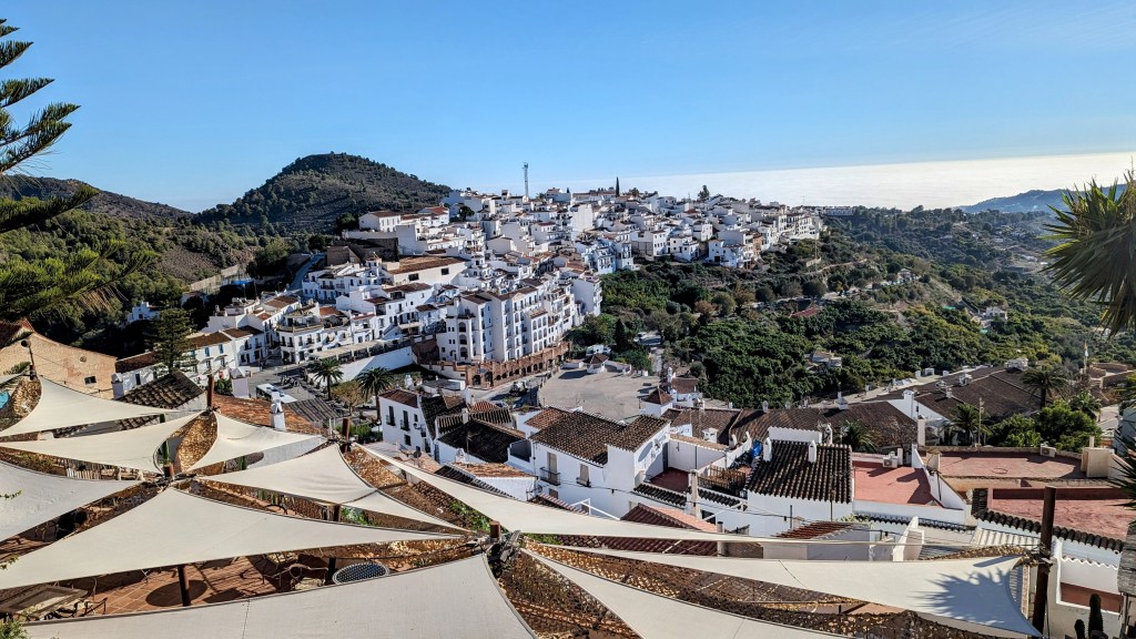 Panoramic view of Frigiliana showcasing white-washed buildings against a mountainous backdrop, with a glimpse of the coastline in the distance.